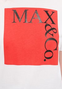 Hvit bomulls t-skjorte med et rødt blokkdesign og teksten "MAX & Co." i fet svart skrift, som har en jevn tekstur.