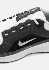 Schwarz-weißes Sneaker mit strukturiertem Obermaterial, silbernem Nike-Swoosh, gepolsterter Zunge und dekorativen Nähten. Verfügt über eine dicke weiße Sohle.