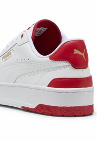 Hvide lædersneakers med røde detaljer på hælen og tungen, med guld-logo, perforerede detaljer og en struktureret rød sål.