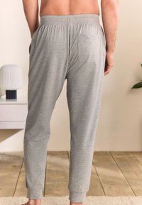 Pantaloni con vita elastica grigia, tasche laterali e una tasca posteriore. Tessuto morbido con texture liscia, vestibilità affusolata ai polsini.
