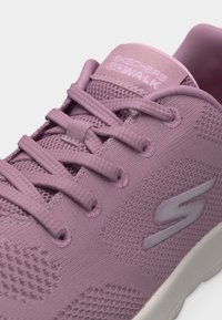 Zapatilla Skechers Go Walk de color lila claro con tejido de punto, cordones redondeados y detalle de suela blanca visible en el lateral.