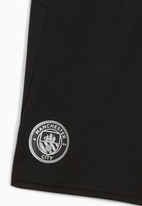 Juodas audinys su „Manchester City“ logotipu, apvalus dizainas su laivu ir rože, esantis kairiajame apatine kampo.