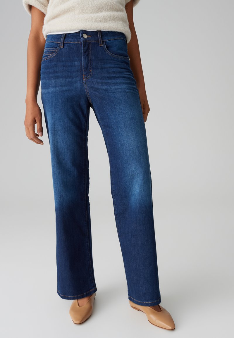 Dunkelblaue Denim-Jeans mit geradem Bein Design, Fronttaschen und subtiler Waschung. Mit goldenen Nähten und einem Metallknopfverschluss.