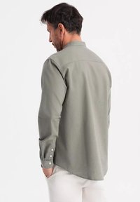 Camicia a maniche lunghe con colletto in tessuto verde opaco, con polsini abbottonati e orlo dritto, mostrata da dietro.