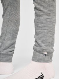 Unterschenkel mit hellgrauer Hose und weißen Socken mit sichtbarem schwarzem Logo-Schriftzug auf den Socken und einem bienenförmigen Anhänger an der Hose.