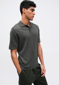 Kohlegraues Poloshirt mit klassischem Kragen, kurzen Ärmeln und einer weichen Textur. Getragen mit dunkelgrünen Cordhosen.