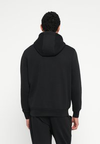Zwarte hoodie met een grote capuchon, geribbelde manchetten en zoom. Gemaakt van zachte, gestructureerde stof met een ontspannen pasvorm en minimale naden.