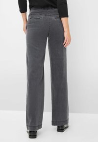 Grijze wijde jeans van denim, met een platte tailleband, achterzakken en een rechte snit tot aan de zoom, die over zwarte schoenen rust.
