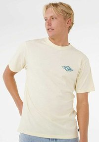 Cremefarvet kortærmet t-shirt lavet af blødt stof, med et lille blåt logo på brystet og en rund halsudskæring.