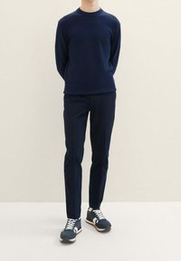 Marinblå strukturerad tröja, marinblå slim-fit byxor och marinblå sneakers med vita accenter. Outfiten har en enkel design och en slimmad silhuett.
