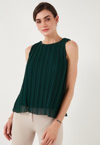 Smaragdgrøn ærmeløs bluse med lodrette plisseringer, rund halsudskæring og gennemsigtig bundkant; letvægtsstof, svævende materiale og minimalistisk design.