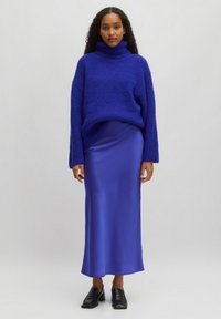 Over sized gestructureerde blauwe gebreide coltrui, gecombineerd met een elegante satijnen blauwe midi rok. Zwarte loafers met blokhak maken de outfit compleet.
