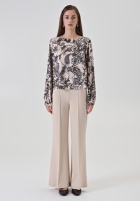 Maglietta a maniche lunghe beige con motivo paisley nero; abbinata a pantaloni larghi beige. Tessuto liscio, vestibilità comoda, design minimalista.