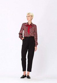 Blouse florale bordeaux à manches longues avec un col noeud, associée à un pantalon noir taille haute et des mocassins noirs, sur un fond uni.