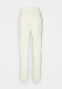 Crèmegekleurde sweatpants met een elastische tailleband, taps toelopende broekspijpen en elastische boorden bij de enkels. Zacht materiaal met een gladde textuur.