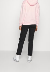 Hoodie rosa chiaro con vestibilità ampia e cappuccio con stringhe, abbinato a pantaloni neri slim-fit e sneakers alte bianche.