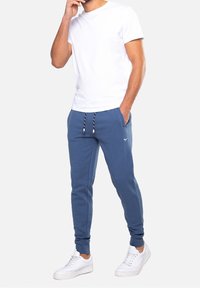 Modré teplákové kalhoty z bavlny s elastickým pasem a šňůrkou. Kombinovány s jednoduchým bílým tričkem s krátkým rukávem a bílými teniskami.