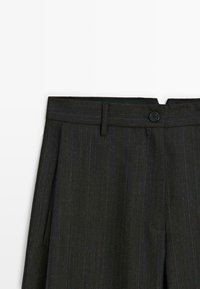 Zwarte pinstripe op maat gemaakte broeken met een knoop en riemlussen bij de tailleband, gezien van voor de taille naar beneden.