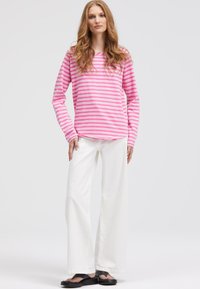 Langarmoberteil in Rosa und Weiß mit Streifen, kombiniert mit weißen, weiten Hosen und schwarzen Sandalen. Glattes Material, lockere Passform, lässiges Design.