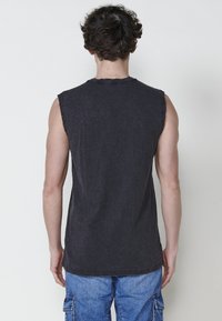 Ärmlös svart linne i mjuk bomullstok med råa kanter, parat med ljusblå cargoshorts med flera fickor.