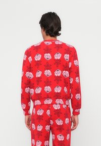 Felpa rossa con motivo floreale in tonalità di rosa e nero, con polsini e vita a coste, realizzata in tessuto morbido.
