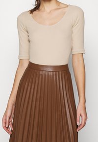 Beige geribbelde top met een ronde hals en korte mouwen, gecombineerd met een bruine geplooide leren rok met een hoge, glanzende tailleband.