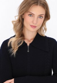 Maglione zip-up blu navy con una maglia testurizzata, caratterizzato da un ampio colletto e una piccola cerniera in metallo. Dettaglio a trecce lungo i lati.