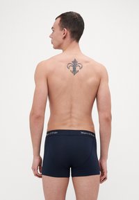 Boxer in blu navy realizzati in materiale morbido con una vestibilità aderente. La vita presenta il logo "Marc O'Polo". Il modello ha un tatuaggio sulla schiena.