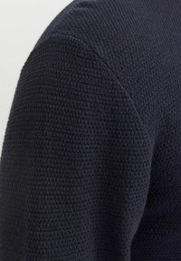 Sweater de punto azul marino con un patrón texturizado, que presenta un cuello redondo y mangas raglán, mostrando un material suave y transpirable.