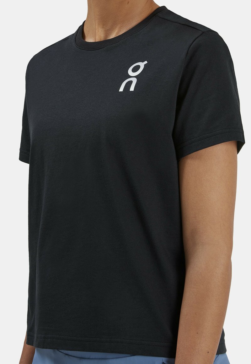 Black cotton T-shirt with short sleeves, round neckline, and a white logo on the left chest. Soft texture and relaxed fit.