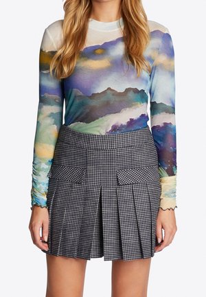 Femme portant un haut à manches longues avec des couleurs abstraites de montagne et une jupe plissée à carreaux noir et blanc avec des poches devant.