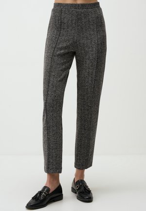 Pantalon droit gris texturé porté avec des mocassins noirs à pampilles sur une personne debout devant un fond clair uni.