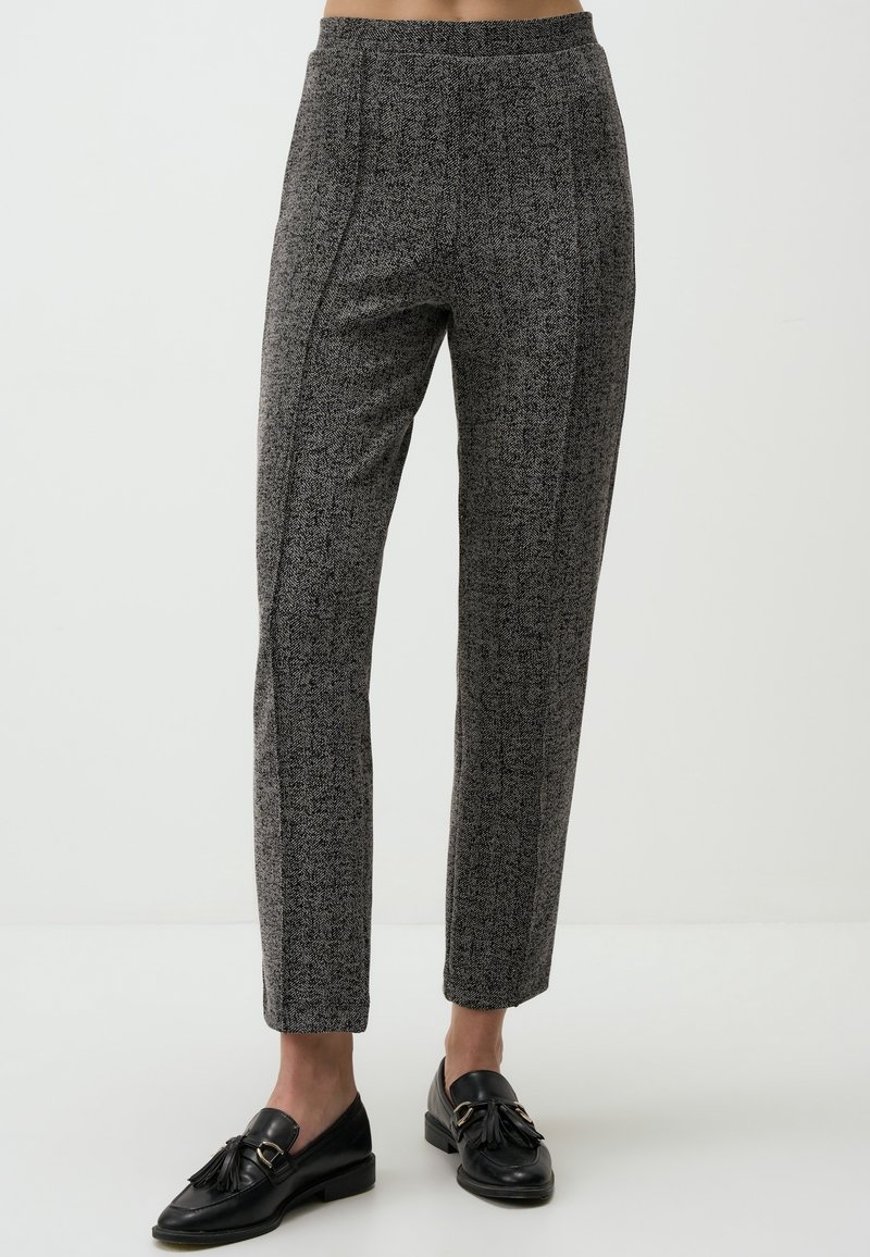 Pantalon droit gris texturé porté avec des mocassins noirs à pampilles sur une personne debout devant un fond clair uni.