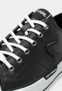 Μαύρο δερμάτινο αθλητικό παπούτσι με λευκά κορδόνια και οφθαλμούς. Διαθέτει ανασηκωμένη μαύρη λογότυπο και ετικέτα με τη μάρκα στην πλευρά.