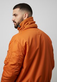 Orange bomber jacket with a textured, knitted collar. Features a zip pocket on the sleeve and sleek, shiny fabric.