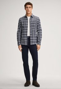 Camicia a quadri nei colori navy, bianco e grigio, abbinata a pantaloni blu scuro e stivali alla caviglia marroni. Design slim fit, stile casual.