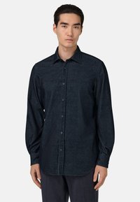 Camicia a maniche lunghe di colore blu scuro realizzata in tessuto texturizzato, con chiusura bottonata, colletto a punta e orlo curvo.
