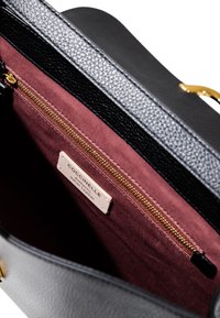 Borsa in pelle nera testurizzata, aperta per rivelare un rivestimento bordeaux con una tasca con zip e un'etichetta che recita "Coccinelle Autentica Pelle Italiana."