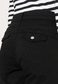 Zwarte stretchjeans met een slim fit, voorzien van een hoge tailleband, twee achterzakken met zilveren drukknopen en een gladde textuur.