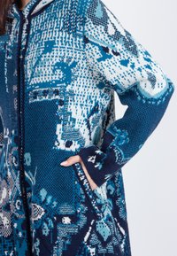 Gebreide hoodie cardigan in blauw en witte patronen met zakken, met een mix van texturen en ingewikkelde ontwerpen.
