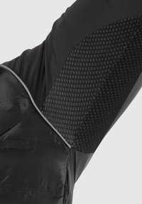 Schwarze Pufferjacke mit Ärmeln, die ein strukturiertes Mesh-Panel, glatte Stoffakzente und einen reflektierenden Besatz entlang der Nähte aufweisen.