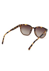 Gafas de sol de carey con lentes degradados, forma angular y brazos delgados. El marco texturizado presenta acentos en amarillo y marrón.