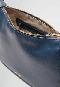 Blaue Lederhandtasche mit glatter Textur und goldfarbener Reißverschluss. Das Innere ist mit einem hellbeigen Futter mit subtilen Mustern versehen.