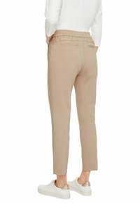 Pantalons beiges légers et fuselés avec une taille élastique et deux poches arrière, associés à des baskets blanches.