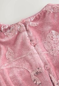 Roze fluwelen jurk met ingewikkelde pailletten bloemdecoraties, kleine ronde knoopsluitingen bij de halslijn en een zachte textuur.