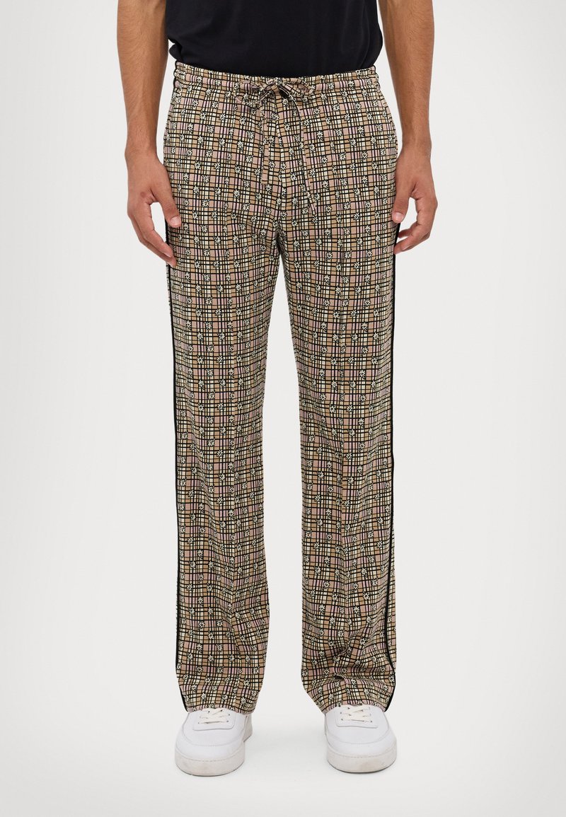 patterned pants with beige and black geometric design, drawstring waist, side black stripes, and breathable fabric. White sneakers worn.