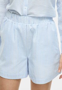 Shorts rayés bleu clair et blanc avec une taille élastique et des poches latérales ; le tissu semble doux avec une texture lisse.