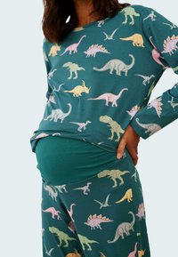 Långärmad turkos loungewear-set med en mängd färgglada dinosauriemönster. Mjuk tyg med en figurnära passform och elastiskt midjeband.