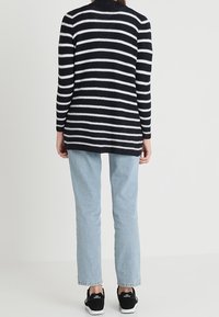 Granatowo-biały, paskowany sweter z długim rękawem o luźnym kroju, zestawiony ze światło-niebieskimi dżinsami i czarnymi trampkami. Miękka dzianina.