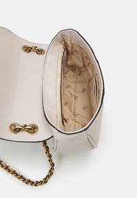 Beige håndtaske lavet af glat materiale med kæde-strop i guldtoner. Indeholder et interiør med beige for og logo-mønster, samt en lynlås-lomme.